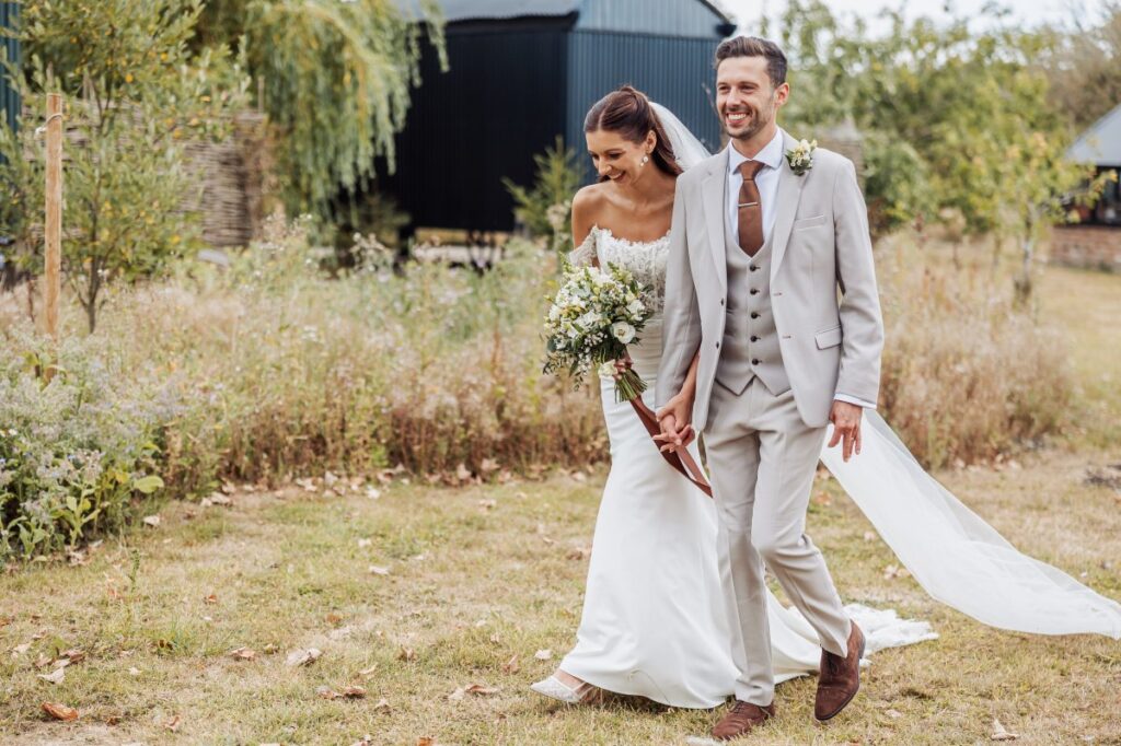 The couple walk together past the black timber barn, the bride's veil catching the wind.