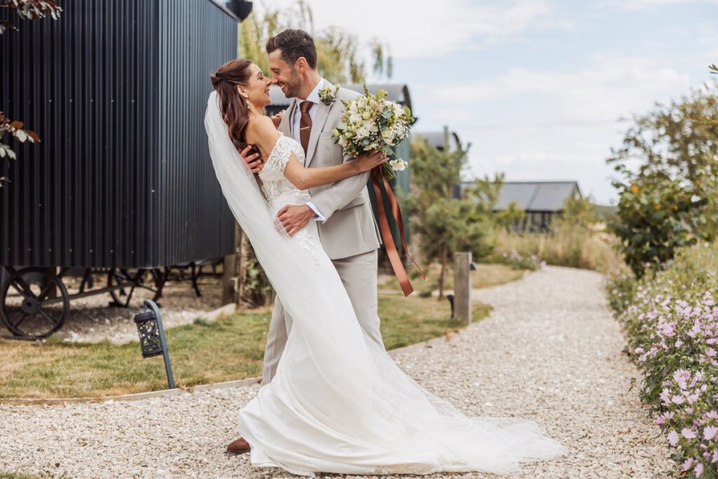 The groom dips his bride for a kiss beside the black barn at Clayfield Farm.