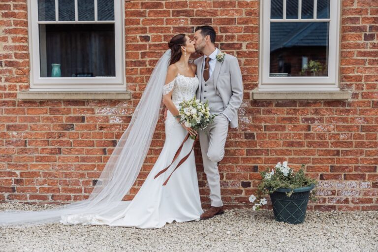 The couple share a kiss against the red brick of the farmhouse at Clayfield Farm.